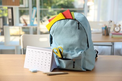 Photo of Backpack with different stationery and calendar on desk in classroom