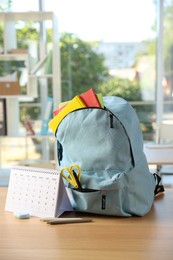 Photo of Backpack with different stationery and calendar on desk in classroom