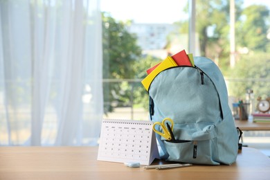 Photo of Backpack with different stationery and calendar on desk in classroom. Space for text