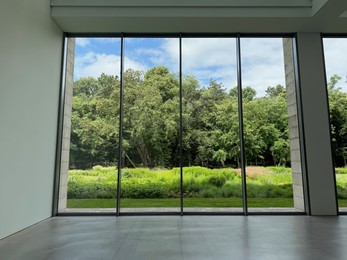 Photo of Beautiful green trees and other different plants under blue sky, view through panoramic windows