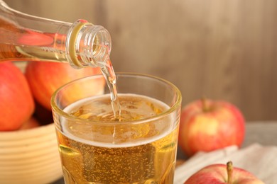 Photo of Pouring delicious apple cider from bottle into glass on blurred background, closeup