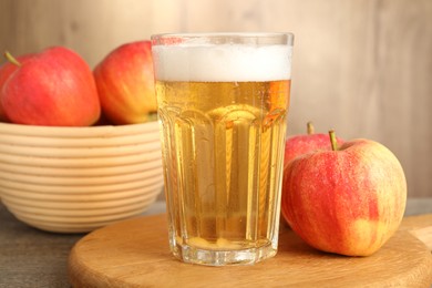 Photo of Delicious cider in glass and apples on wooden table, closeup