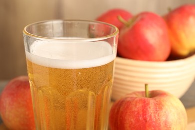 Photo of Delicious cider in glass and apples on blurred background, closeup