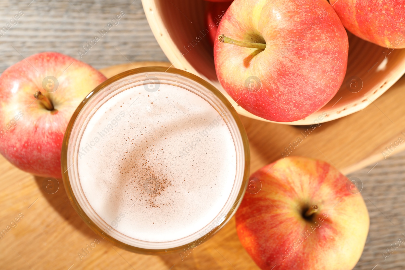 Photo of Delicious cider in glass and apples on wooden table, flat lay