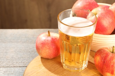 Photo of Delicious cider in glass and apples on wooden table, closeup