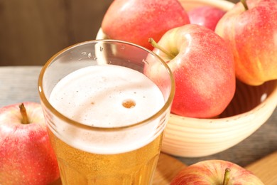 Photo of Delicious cider in glass and apples on table, closeup