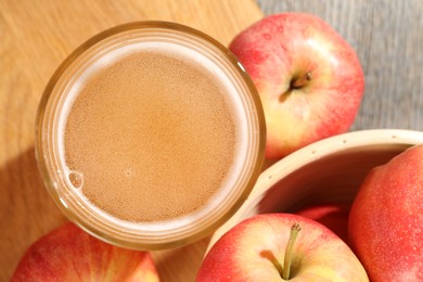 Photo of Delicious cider in glass and apples on wooden table, flat lay