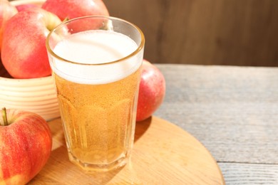Photo of Delicious cider in glass and apples on wooden table, closeup