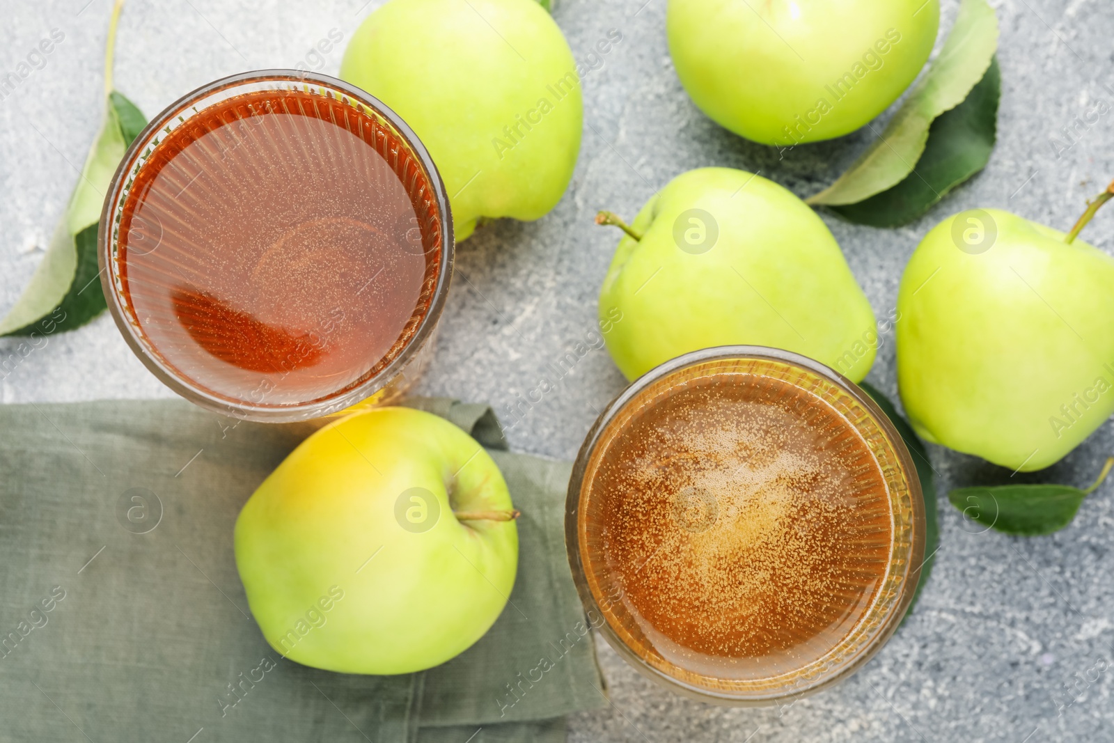 Photo of Delicious cider in glasses, apples and leaves on grey textured table, flat lay