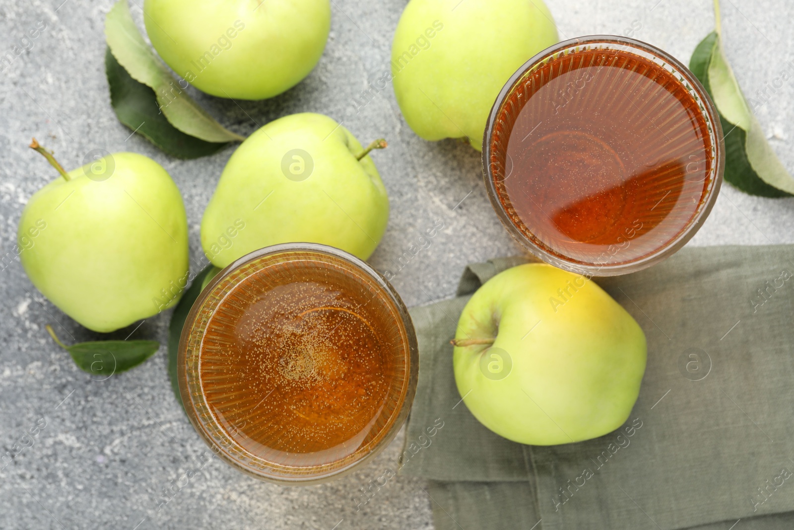 Photo of Delicious cider in glasses, apples and leaves on grey textured table, flat lay
