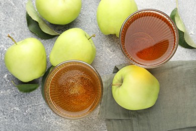 Photo of Delicious cider in glasses, apples and leaves on grey textured table, flat lay