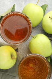 Photo of Delicious cider in glasses, apples and leaves on grey textured table, flat lay