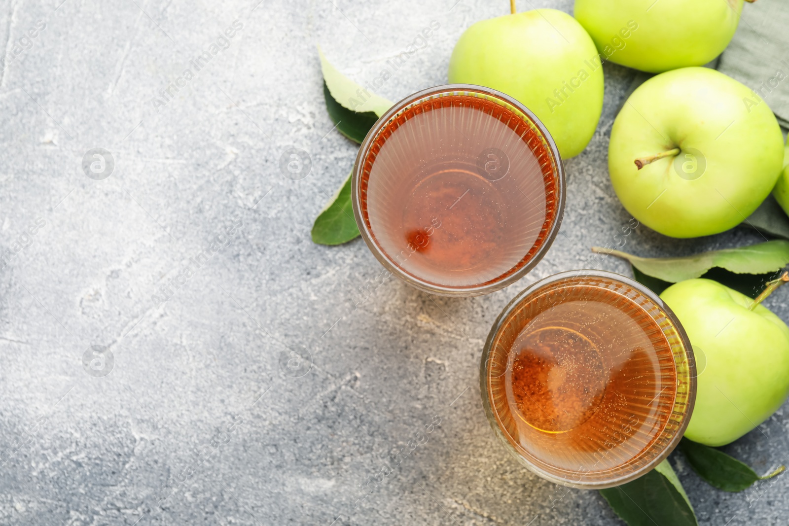 Photo of Delicious cider in glasses, apples and leaves on grey textured table, flat lay. Space for text