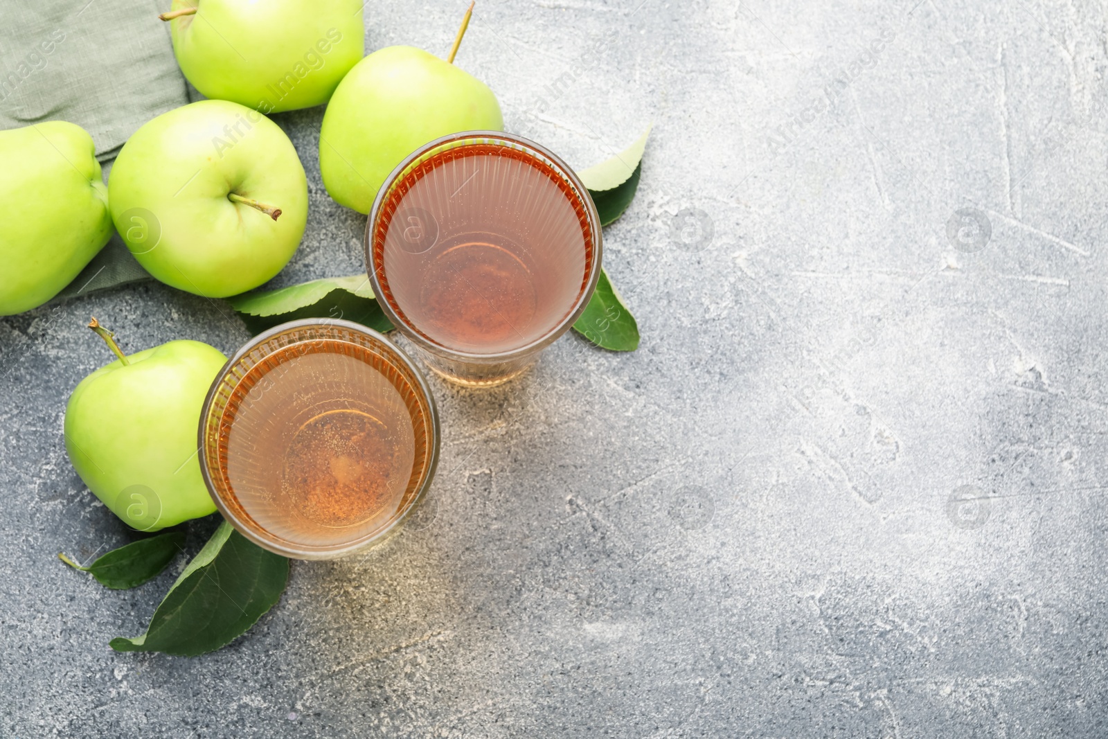 Photo of Delicious cider in glasses, apples and leaves on grey textured table, flat lay. Space for text