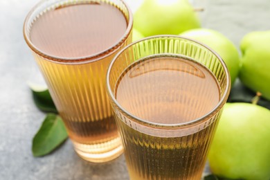 Photo of Delicious cider in glasses, apples and leaves on grey table, closeup
