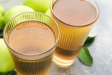 Photo of Delicious cider in glasses, apples and leaves on grey table, closeup