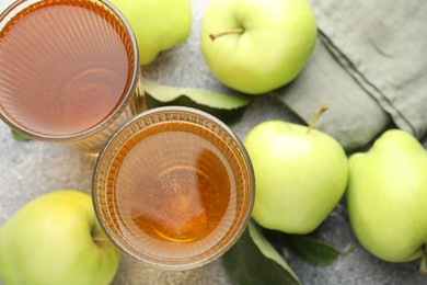 Photo of Delicious cider in glasses, apples and leaves on grey textured table, flat lay