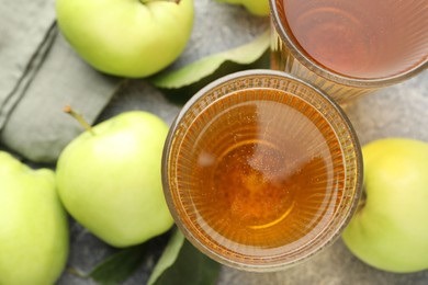 Photo of Delicious cider in glasses, apples and leaves on grey textured table, flat lay