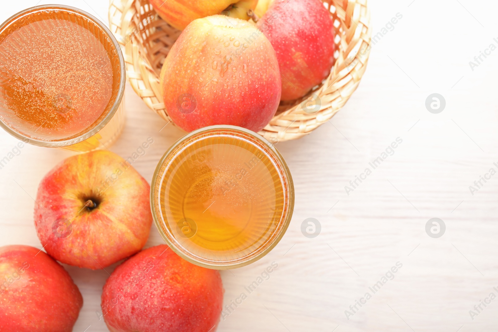 Photo of Delicious cider in glasses and red apples on white wooden table, flat lay. Space for text