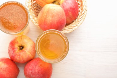 Photo of Delicious cider in glasses and red apples on white wooden table, flat lay. Space for text