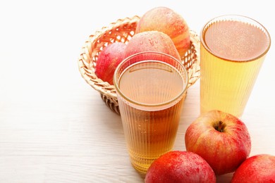 Photo of Delicious cider in glasses and red apples on white wooden table, closeup