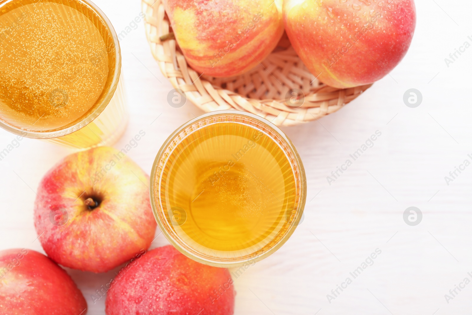 Photo of Delicious cider in glasses and red apples on white wooden table, flat lay