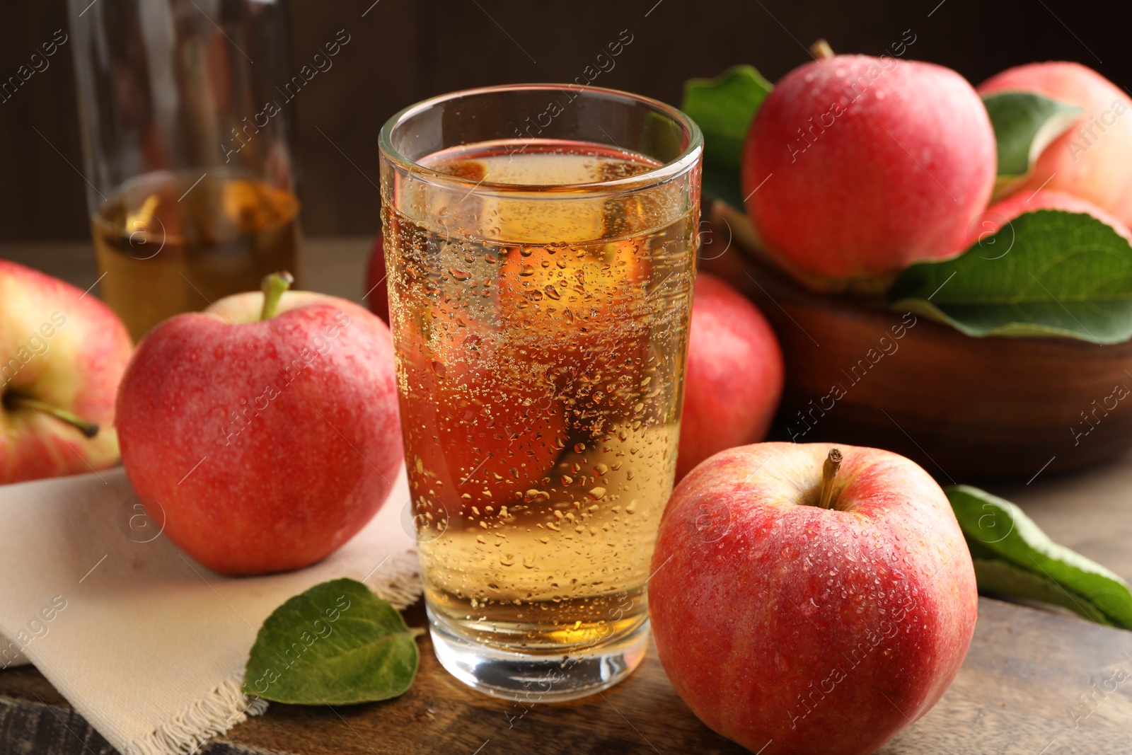 Photo of Delicious cider in glass, apples and leaves on wooden table, closeup