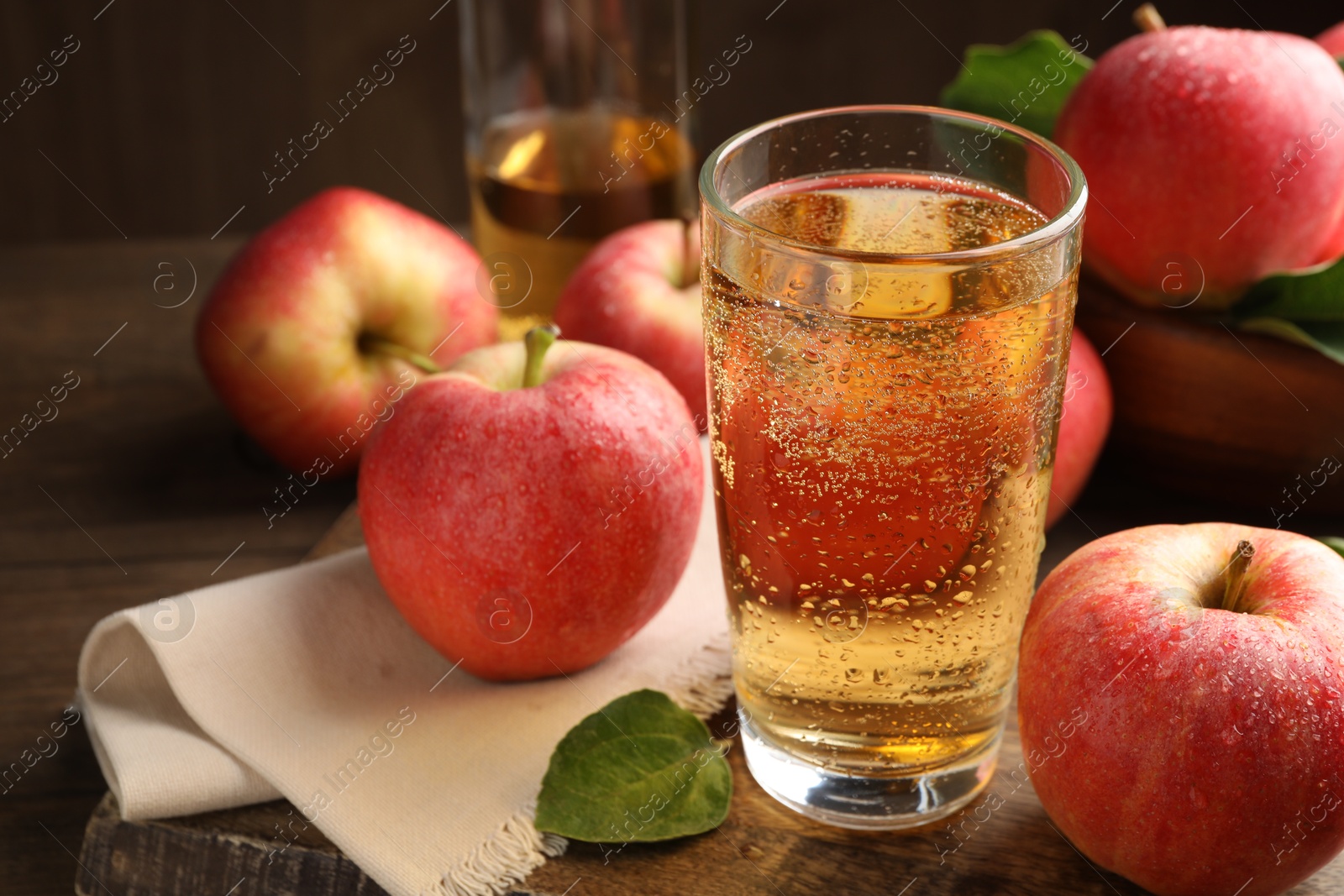 Delicious cider in glass, apples and leaves on wooden table, closeup Photo of Delicious cider in glass, apples and leaves on wooden table, closeup