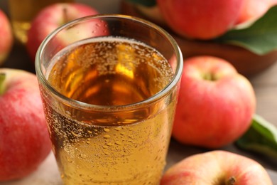 Photo of Delicious cider in glass and apples on table, closeup