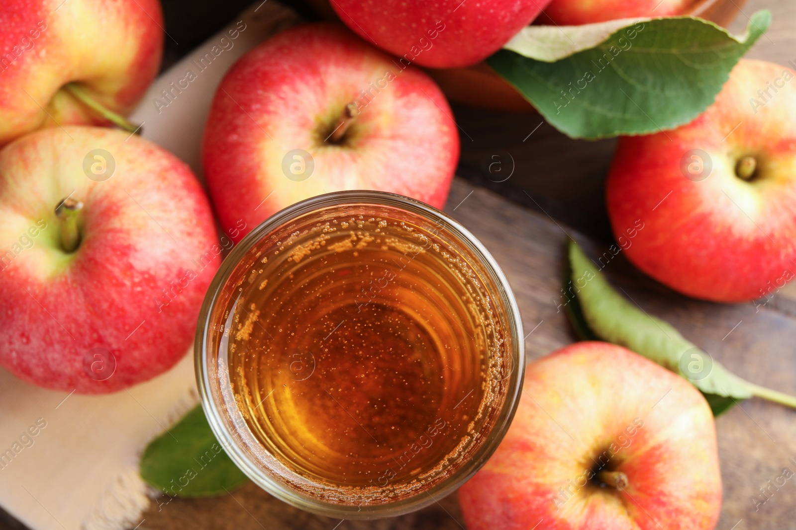 Photo of Delicious cider in glass, apples and leaves on wooden table, flat lay