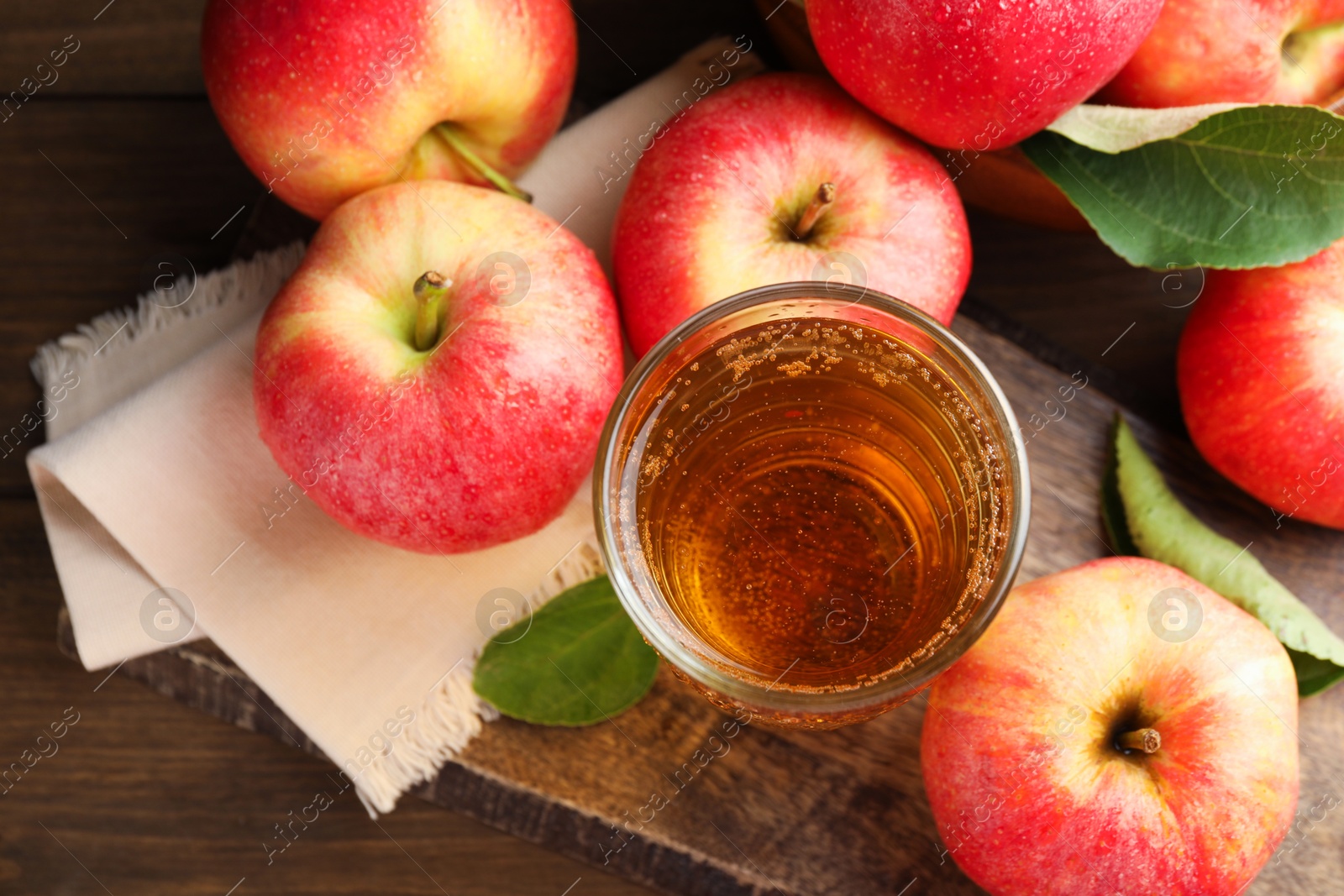 Photo of Delicious cider in glass, apples and leaves on wooden table, flat lay