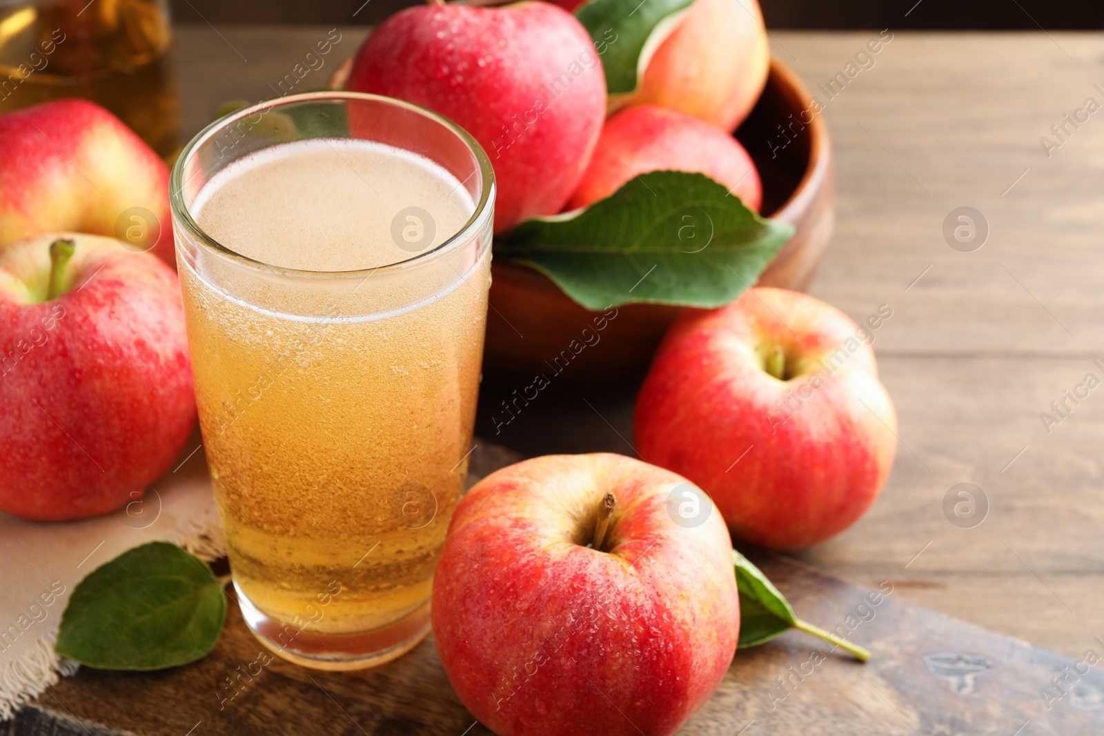 Photo of Delicious cider in glass, apples and leaves on wooden table, closeup