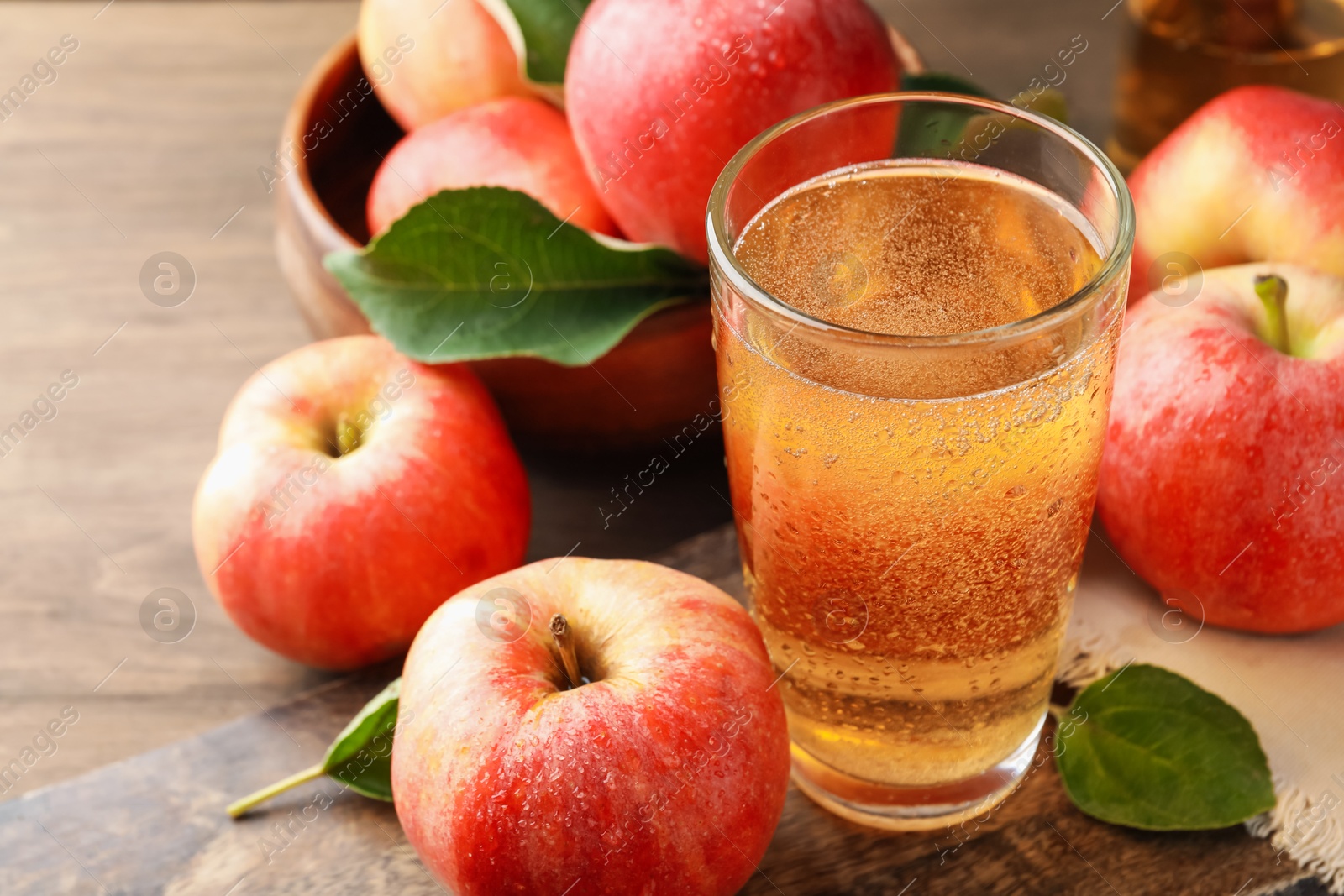 Delicious cider in glass, apples and leaves on wooden table, closeup Photo of Delicious cider in glass, apples and leaves on wooden table, closeup