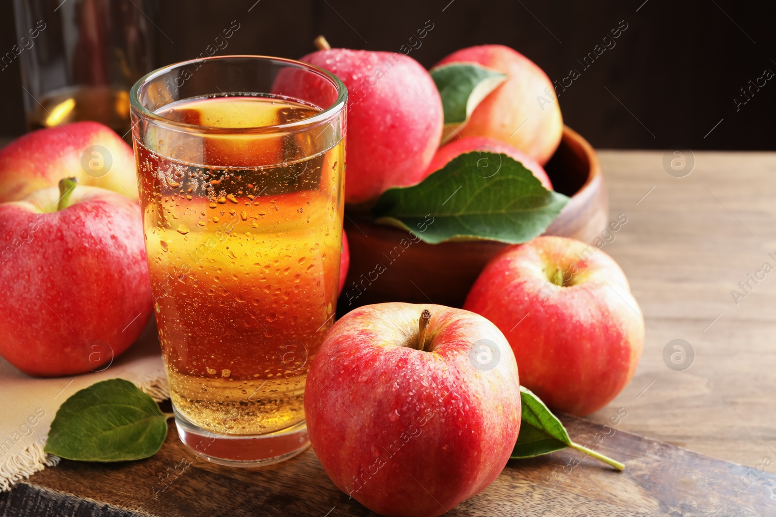 Delicious cider in glass, apples and leaves on wooden table against dark background, closeup Photo of Delicious cider in glass, apples and leaves on wooden table against dark background, closeup