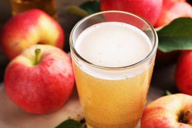 Photo of Delicious cider in glass and apples on table, closeup