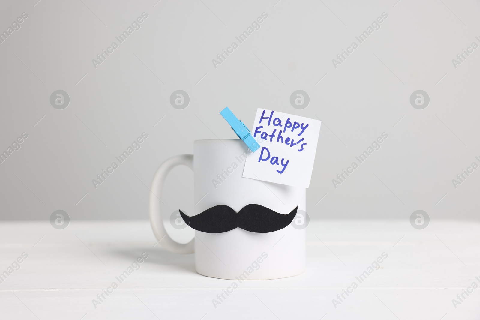 Happy Father's Day. Cup with paper moustache and card on white wooden table Photo of Happy Father's Day. Cup with paper moustache and card on white wooden table