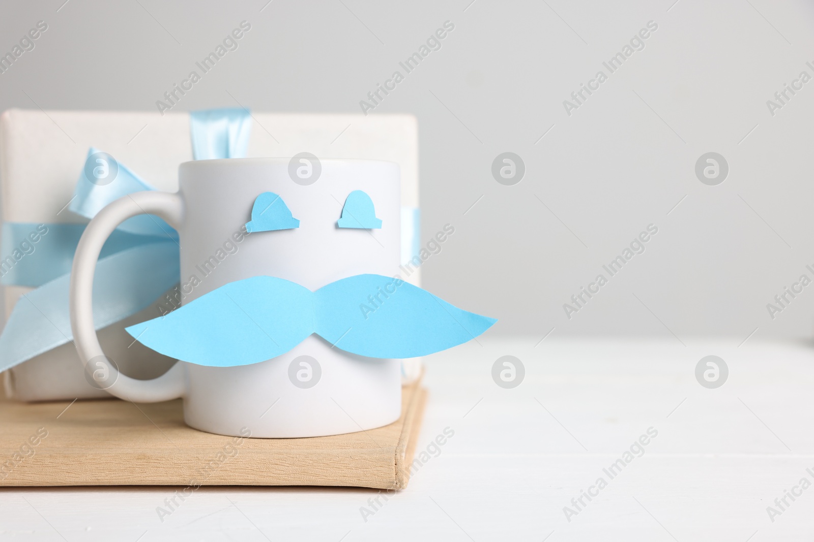 Happy Father's Day. Cup with paper face and gift box on white wooden table, closeup. Space for text Photo of Happy Father's Day. Cup with paper face and gift box on white wooden table, closeup. Space for text