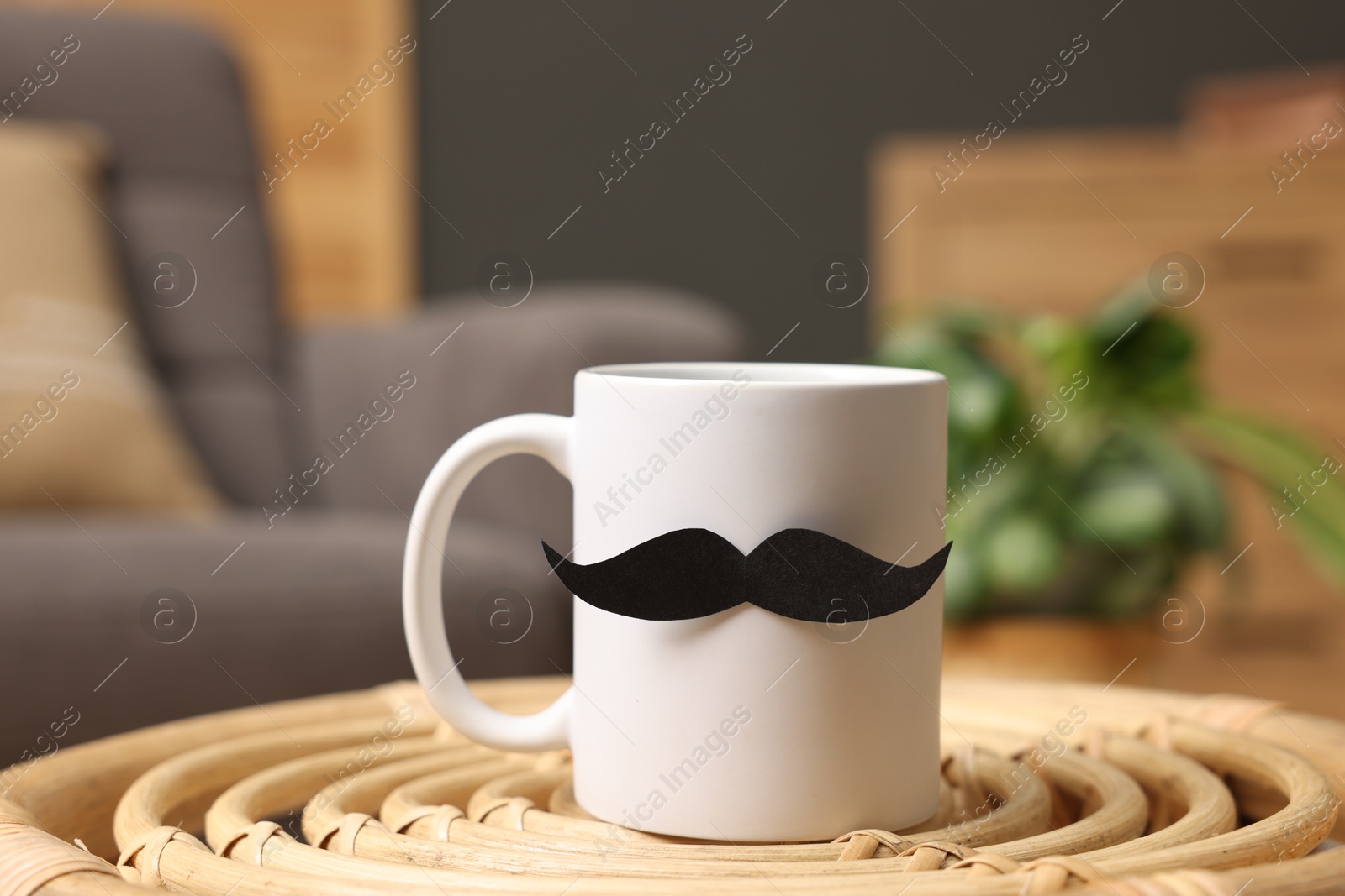 Photo of Happy Father's Day. Cup with paper moustache on coffee table indoors, closeup