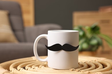 Photo of Happy Father's Day. Cup with paper moustache on coffee table indoors, closeup
