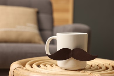 Photo of Happy Father's Day. Cup with paper moustache on coffee table indoors, closeup. Space for text
