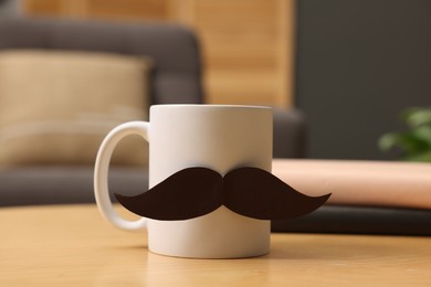 Photo of Happy Father's Day. Cup with paper moustache and books on wooden table indoors, closeup