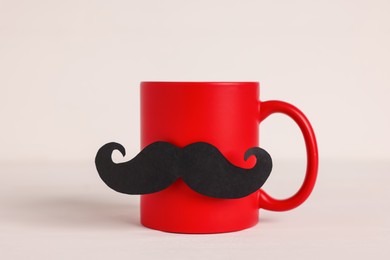 Photo of Happy Father's Day. Cup with paper moustache on white wooden table, closeup