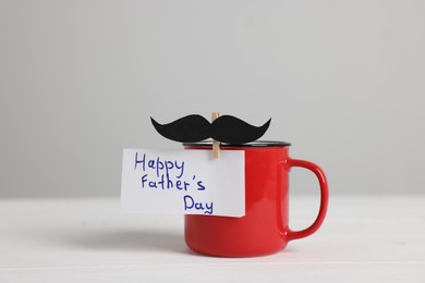 Photo of Happy Father's Day. Cup with paper moustache and card on white wooden table
