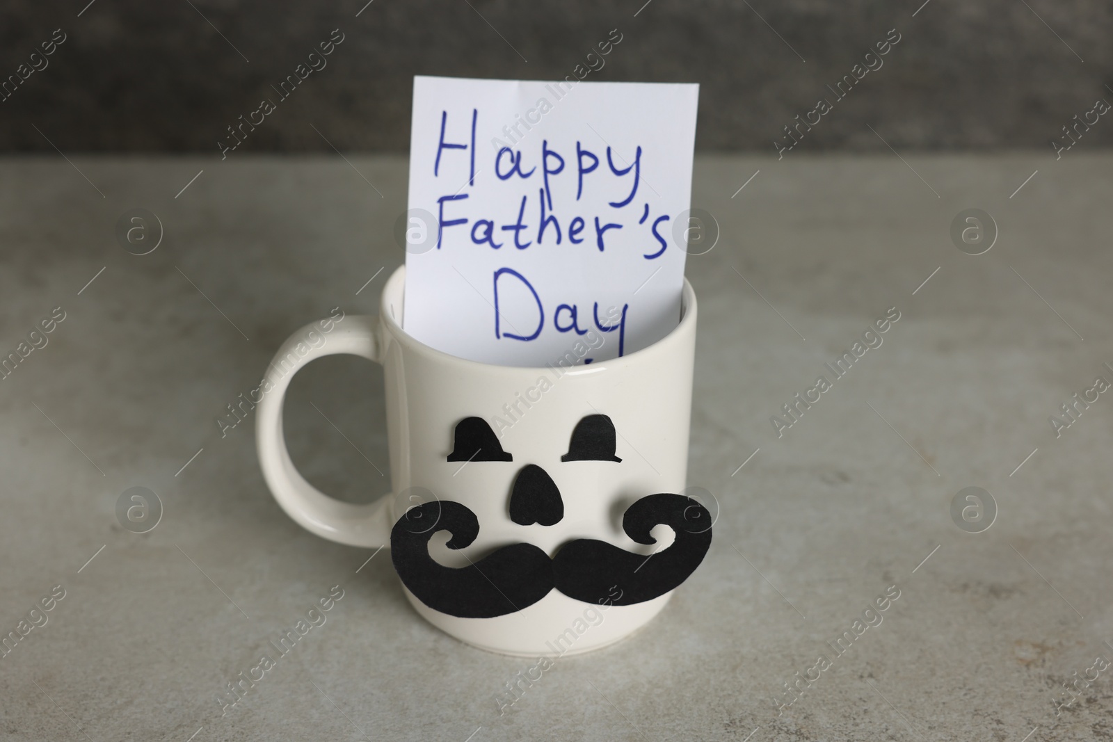 Happy Father's Day. Cup with paper face and card on light grey table, closeup Photo of Happy Father's Day. Cup with paper face and card on light grey table, closeup
