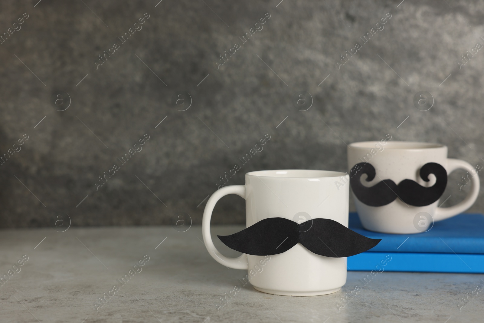 Happy Father's Day. Cups with paper moustaches and books on light grey table, closeup. Space for text Photo of Happy Father's Day. Cups with paper moustaches and books on light grey table, closeup. Space for text