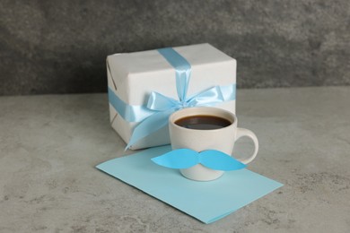 Photo of Happy Father's Day. Cup with paper moustache, gift box and card on light grey table