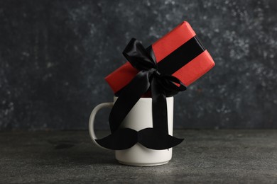 Photo of Happy Father's Day. Cup with paper moustache and gift box on black table