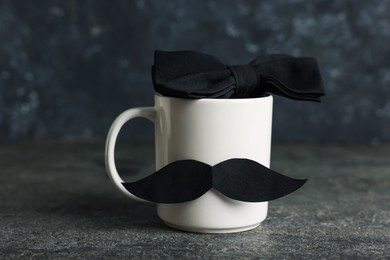 Photo of Happy Father's Day. Cup with paper moustache and bowtie on black table, closeup