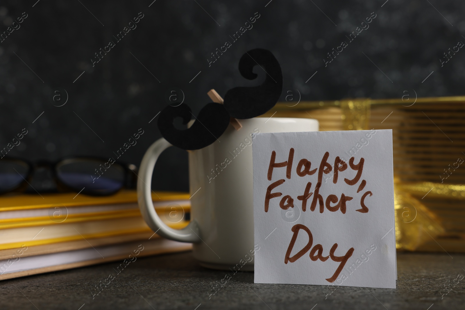 Happy Father's Day. Cup with paper moustache, card, books and gift box on black table, closeup Photo of Happy Father's Day. Cup with paper moustache, card, books and gift box on black table, closeup