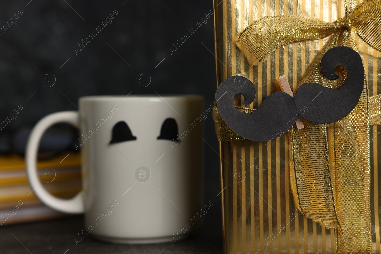Happy Father's Day. Cup with paper face, moustache and gift box on black table, closeup Photo of Happy Father's Day. Cup with paper face, moustache and gift box on black table, closeup